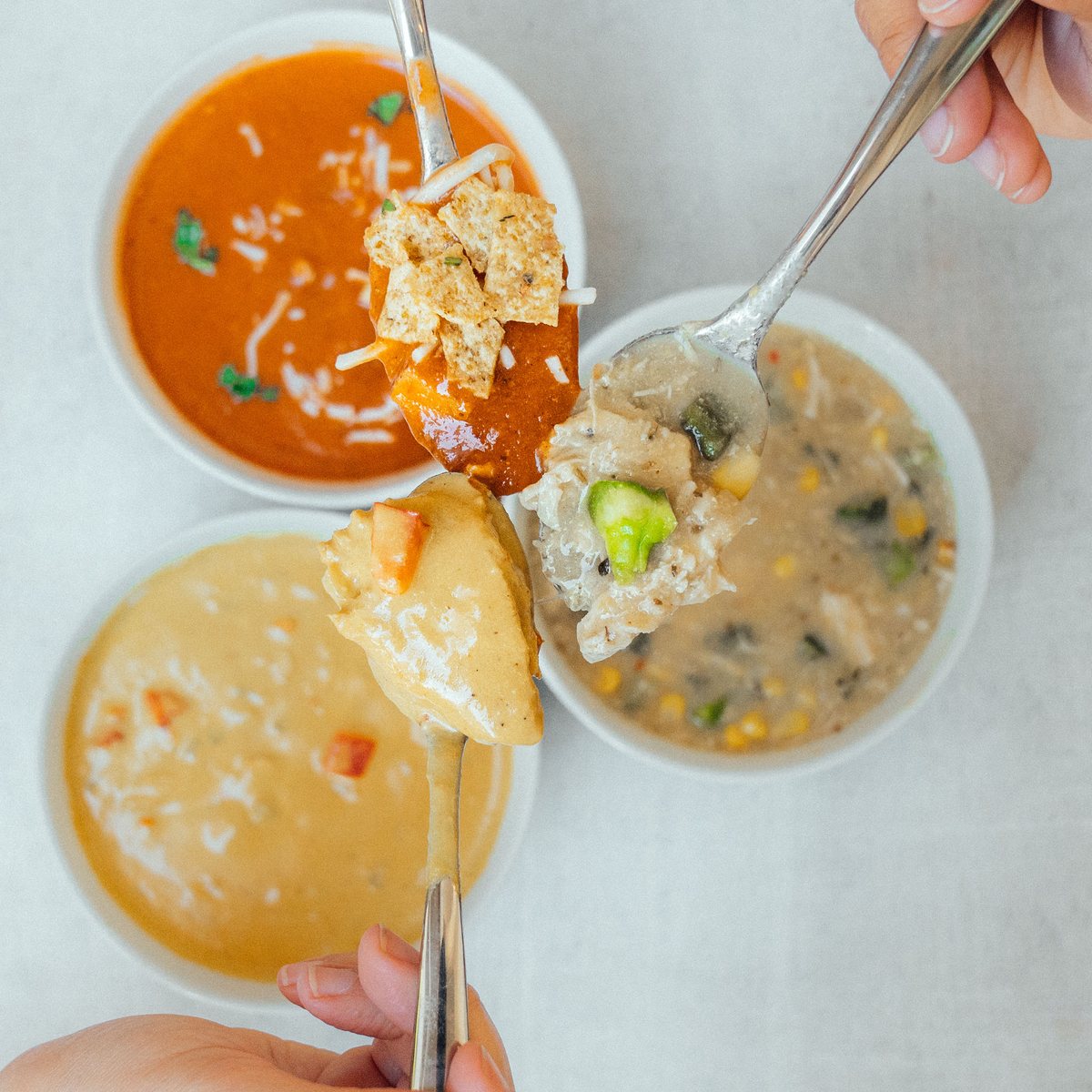 Friends sharing several soups together, spoons meeting over the bowls